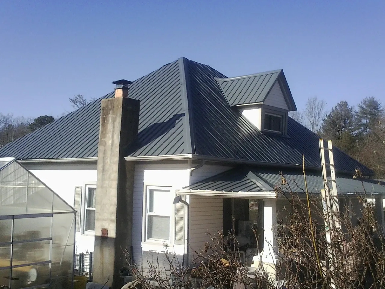 Dark blue standing seam metal roof on a white farmhouse with dormer — Slate & Tile Roof Repair by Roofing Brothers in Wichita Falls