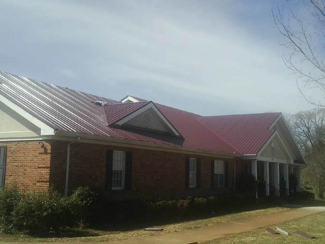 Red metal roof with gabled entries on a long brick building, from a Hail Damage Roof Repair job in Wichita Falls