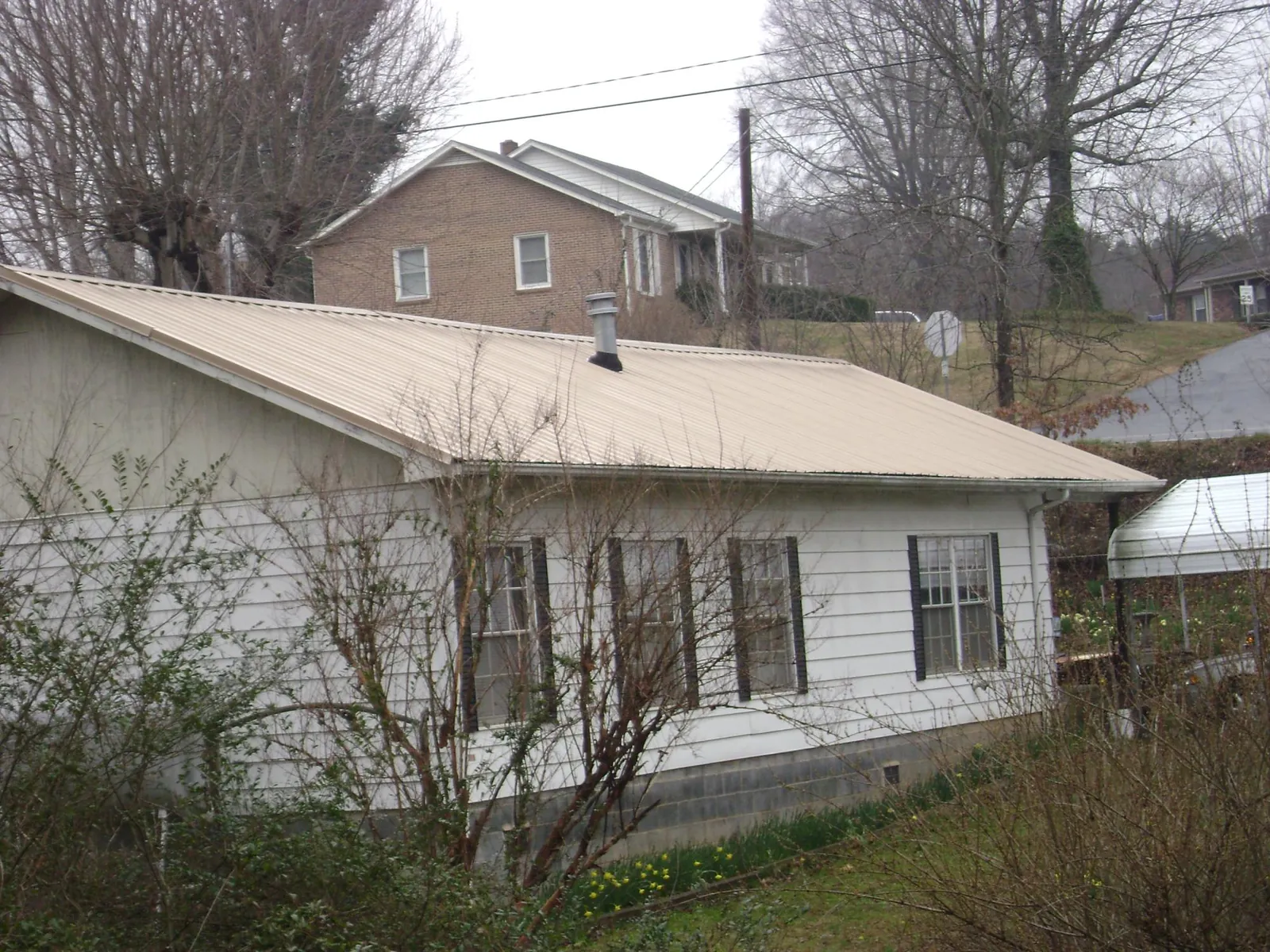 Tan metal roof on a white sided house set into a hillside — Commercial Roofing by Roofing Brothers in Wichita Falls